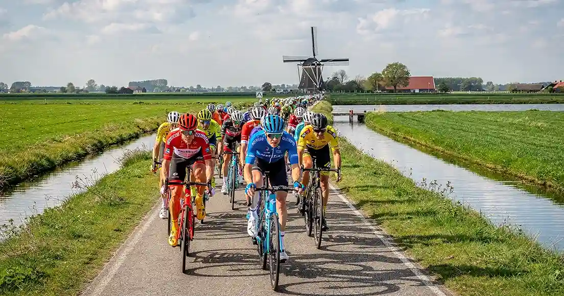 Wielrenners rijden door Nederlands landschap met molen